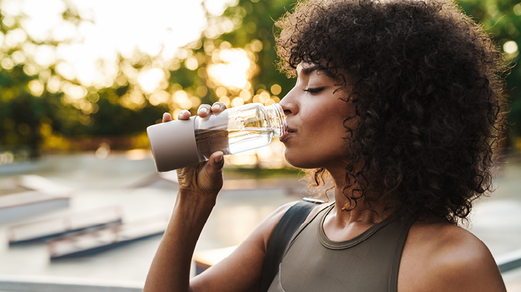 Frau trinkt aus einer Glasflasche Wasser im Freien.