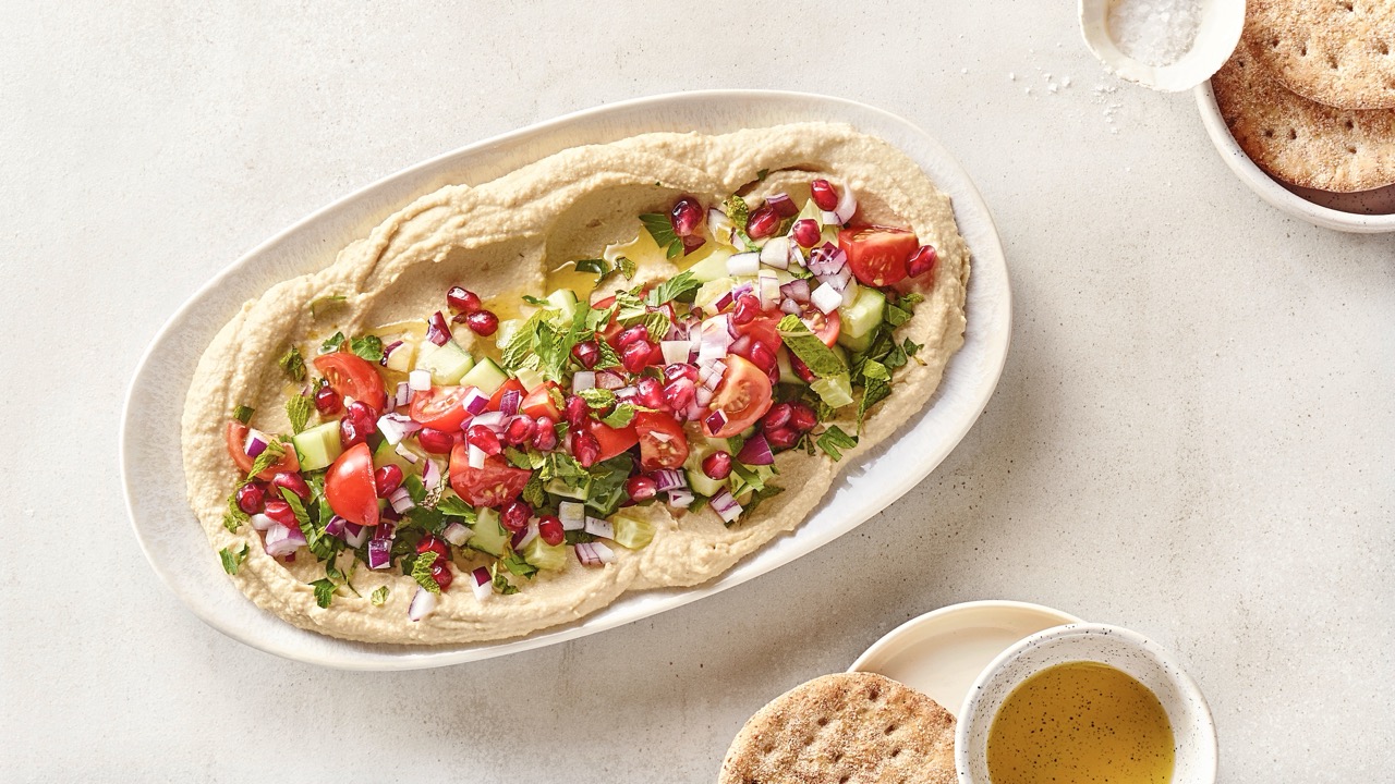 Loaded-Hummus-Bowl-Rezept Eine Schale gefüllt mit Hummus, dekoriert mit Tomaten, Gurke und Granatalpfelkernen