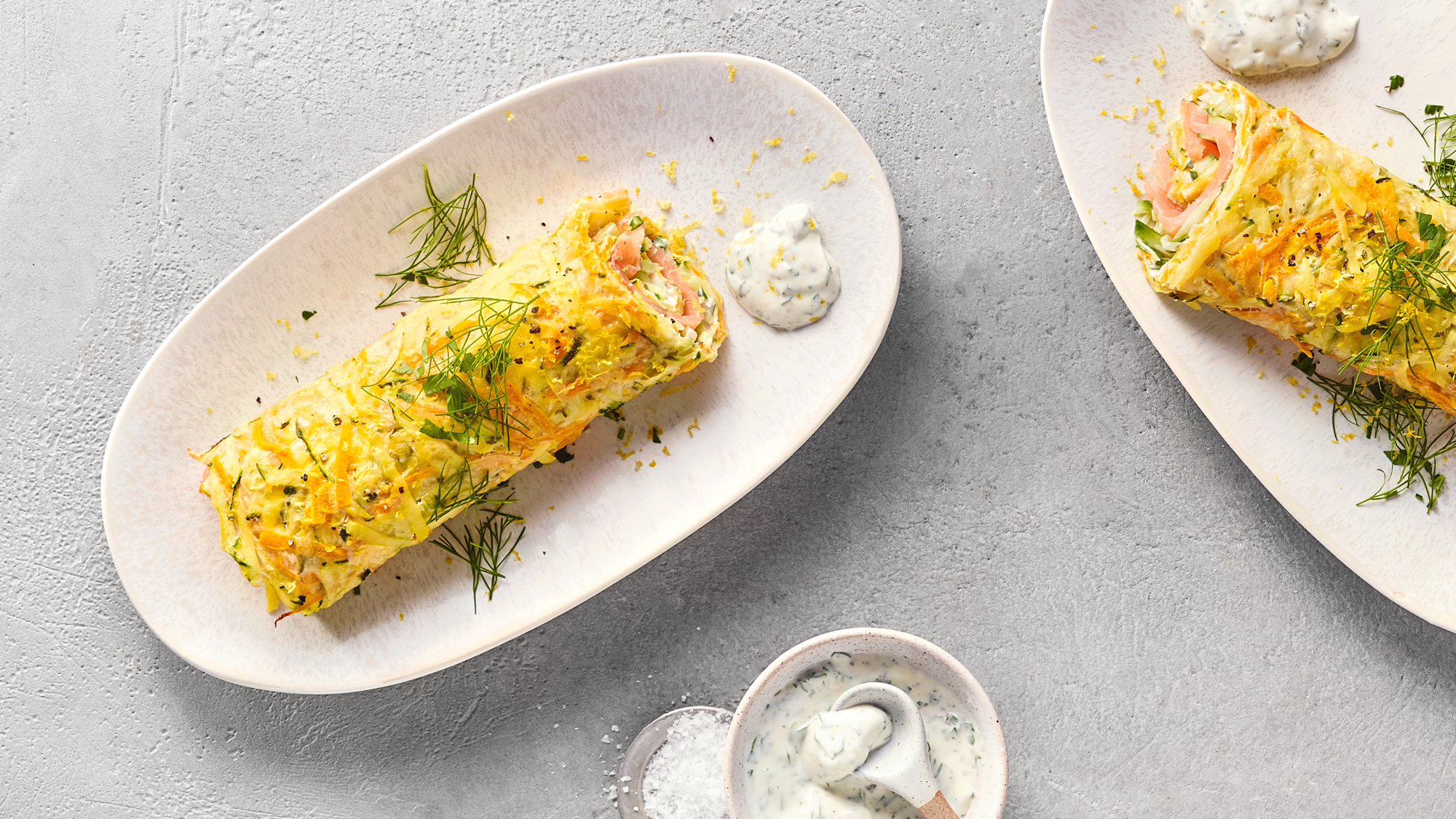 High-Protein-Rolle-Wrap Zwei Gemüse-Wraps auf weißen Tellern mit Dip daneben. Unten in der Mitte steht eine Schüssel mit Dip und Löffel.