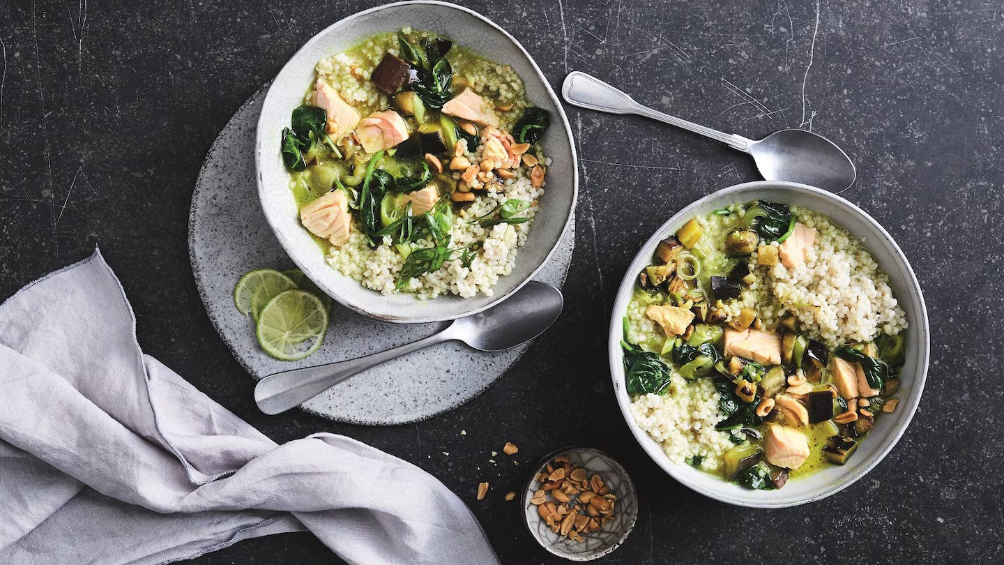 edeka-gruenes-lachs-curry-rezept Zwei Schalen gefüllt mit einem grünen Curry mit Lachs, Perlgraupen und Spinat.