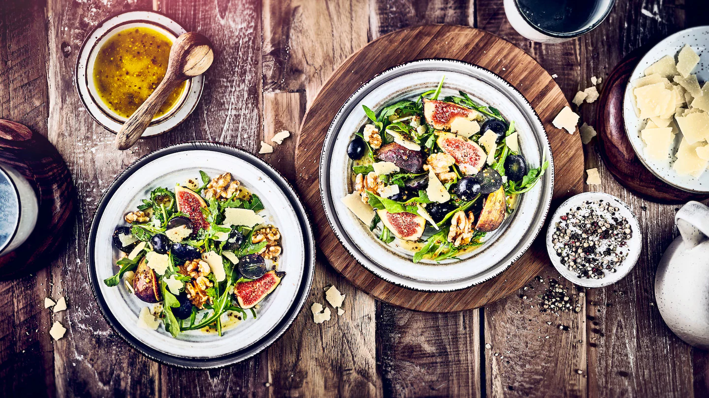 Zwei Teller mit Salat und Feigen, daneben kleinere Schalen mit Dressing und Gewürzen