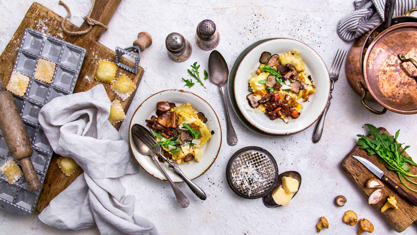 Selbstgemachte Pilz-Ravioli mit gebratenen Pilzen, Trüffel und Parmesan auf zwei Tellern
