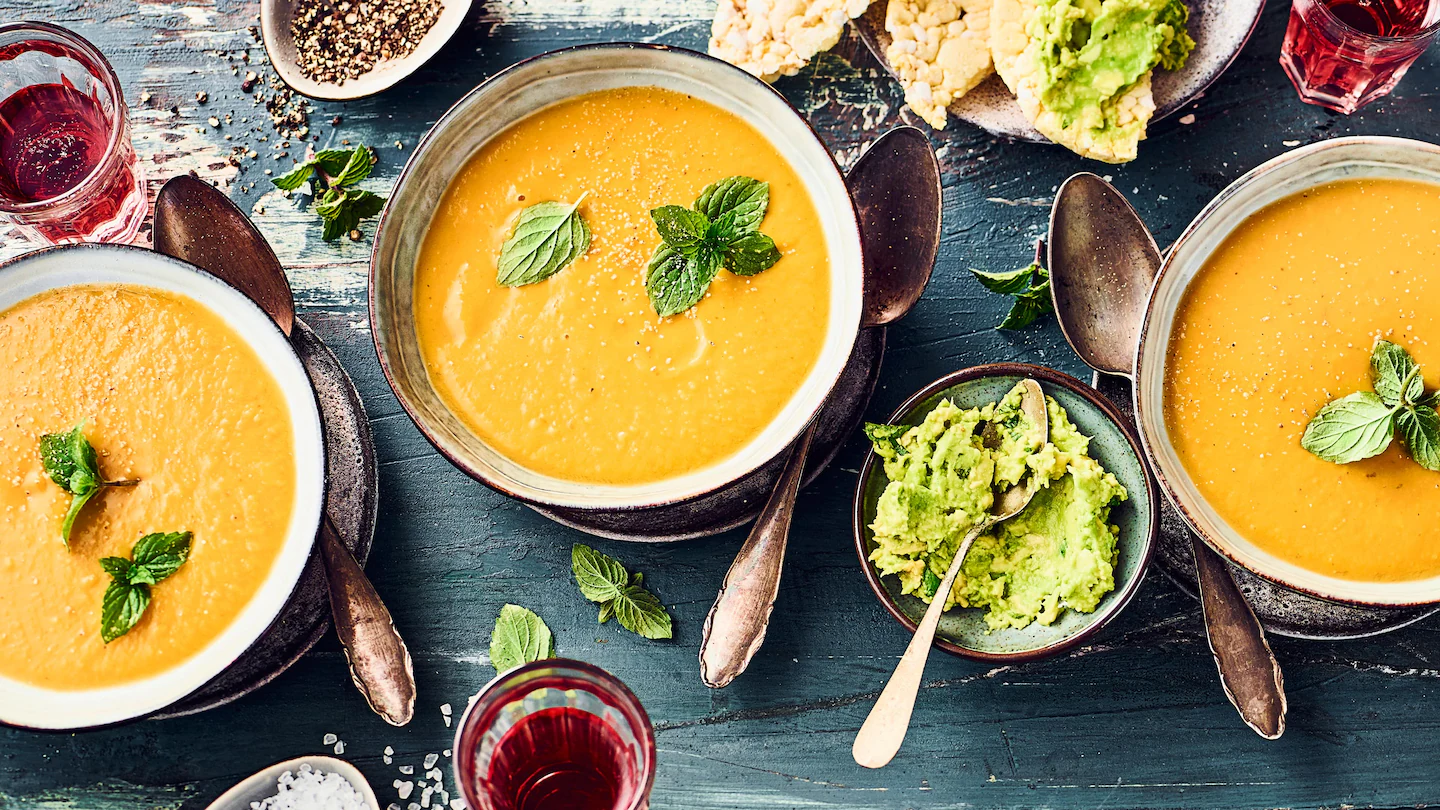 rez-edeka-suesskartoffel-linsen-suppe-rezept-q-t Drei Schalen mir Süßkartoffel-Linsen-Suppe, garniert mit frischer Minze, auf einem dunklen Holztisch.